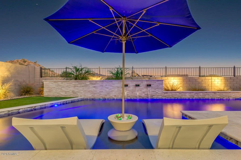 Night pool scene with umbrella, submerged lounge chairs, wall lighting, and blue pool lights