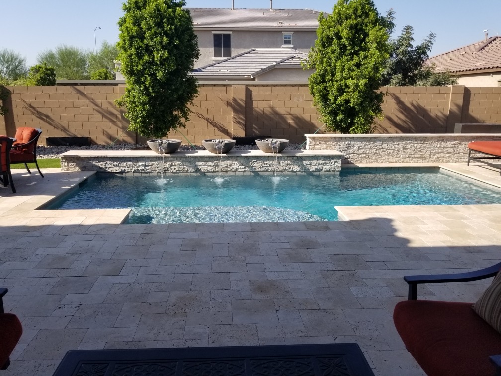 Backyard pool with raised stone wall, three bowl fountains, paver deck, and privacy trees