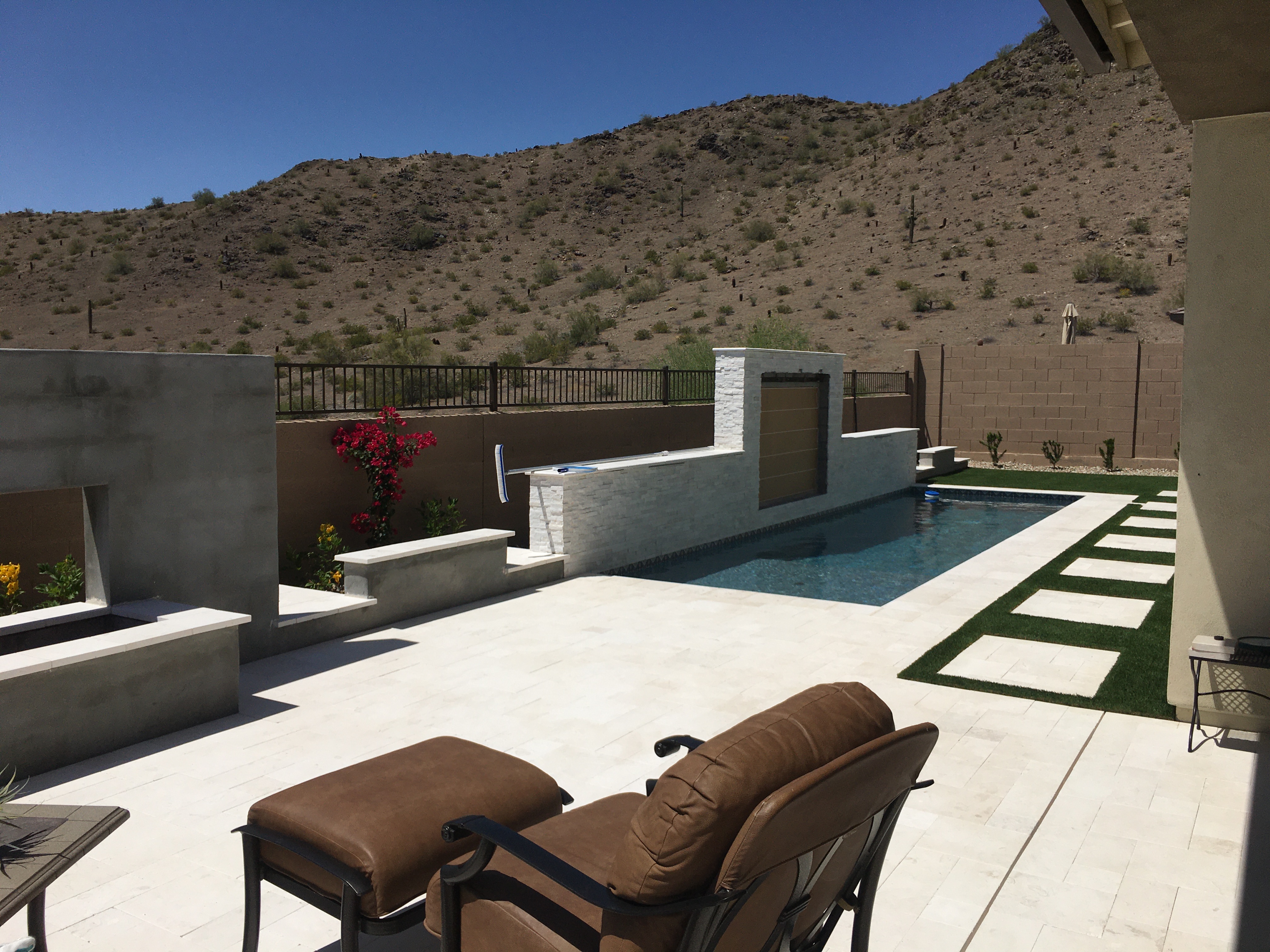 Modern desert backyard pool with water wall, mountain view, paver walkway, and lounge seating